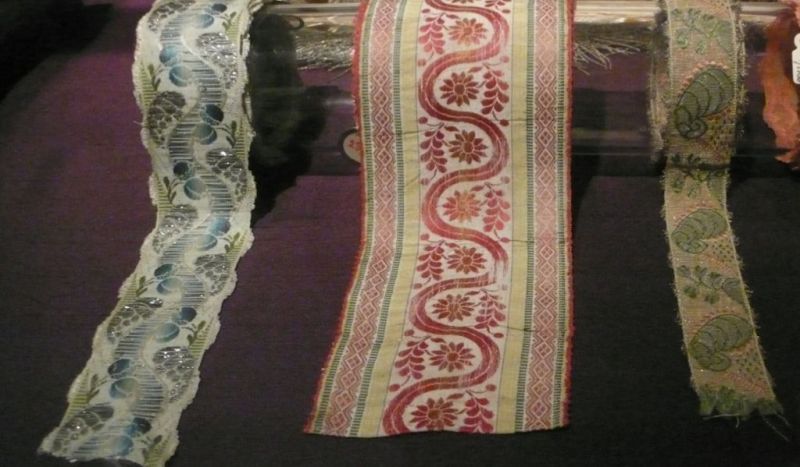 These three complex silk ribbons are probably of French import, used/owned by a wealthy citizen of København [Copenhagen] – a few miles across Öresund from Malmö. However, it is very likely that similar types of exquisite accessories were sold at the previously mentioned merchant Falkman & Suell. The illustrated ribbons originate from the 18th century, woven on multi-coloured silk warps, with weft of silk, gold and silver threads. Techniques include; motif weft, brocading, double weaving and chiné. (Collection: Kunstindustrimuseet,  visit at the exhibition “Fashion & Fabric”). Photo: Viveka Hansen.