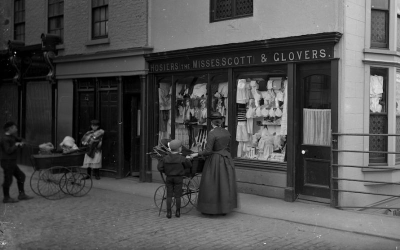 For the 1890 to 1914 period it is easier to find examples of larger and larger display windows in the ever extending department stores in many towns and cities, these snapshots are immortalised in contemporary photographs often with passers-by or via art works or printed advertisements in magazines/newspapers/catalogues. However, even if luxury goods may be associated with window displays most shops in smaller towns arranged ordinary clothing in their windows, like for example The Misses Scott’s establishment in Whitby circa 1895 – a trader described in detail in one of the earlier essays. (Courtesy of: Frank M. Sutcliffe, Whitby Museum, Photographic Collection, part of photograph.)